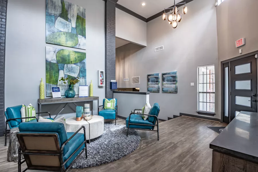 Modern lobby with blue armchairs, abstract art, white coffee table on a grey rug, and a reception desk.