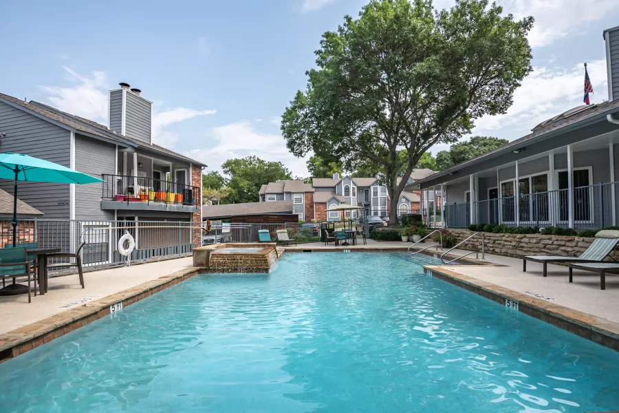 Photograph: Apartment complex pool area with blue water, lounge chairs, and grey buildings under a sunny sky.
