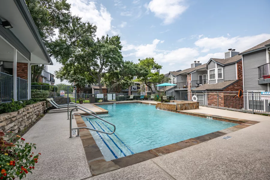 Outdoor swimming pool area with lounge chairs, a hot tub, and modern apartment buildings under a clear sky.