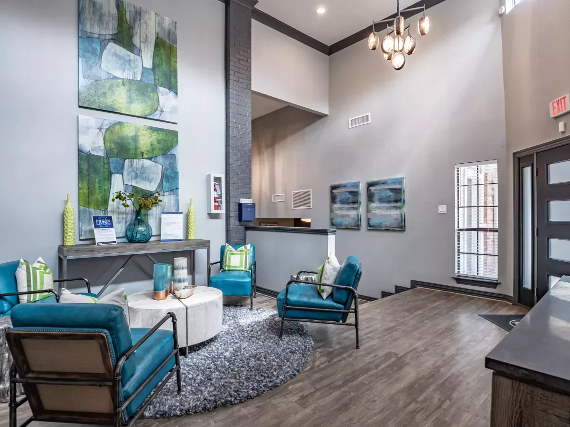 Modern lobby with blue armchairs, abstract art, white coffee table on a grey rug, and a reception desk.