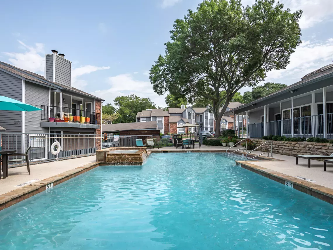 Photograph: Apartment complex pool area with blue water, lounge chairs, and grey buildings under a sunny sky.