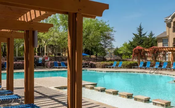 A serene pool area surrounded by lounge chairs, pergolas, and blooming greenery at a residential community.