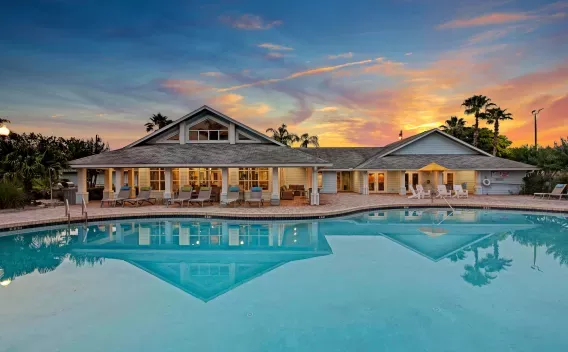 Beautiful clubhouse with large windows and a relaxing pool area at sunset, offering a welcoming ambiance.
