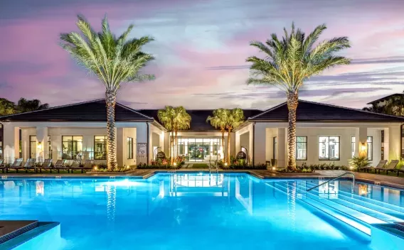 A luxurious resort-style pool illuminated at dusk, surrounded by palm trees and lounge chairs.