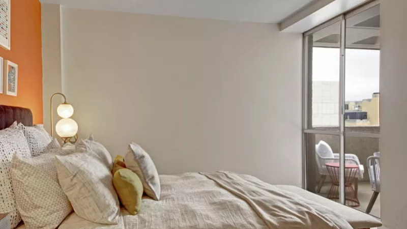 A serene bedroom setup with light-toned bedding and a balcony view.