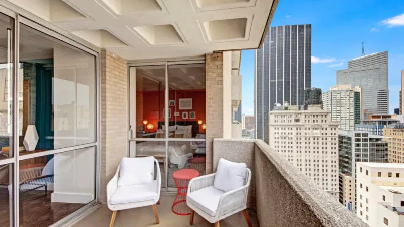  An inviting balcony featuring modern white chairs and a stunning cityscape view.