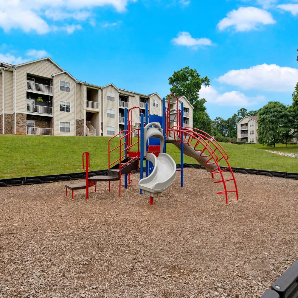 Colorful playground surrounded by lush green grass and modern apartment buildings, offering a fun and safe outdoor space for children to play.