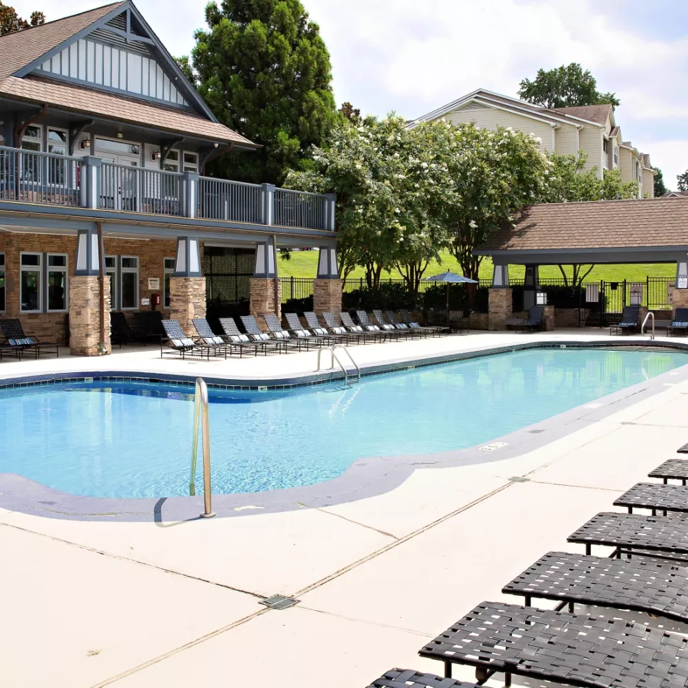 Resort-style swimming pool surrounded by lounge chairs, shaded seating areas, and landscaped greenery, creating a relaxing outdoor oasis for residents.