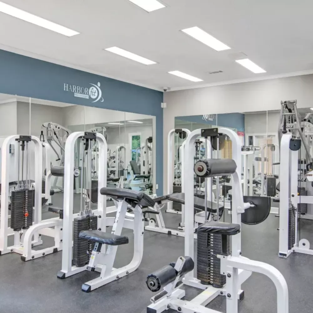 A fully equipped fitness center featuring various strength training machines, a wall of mirrors for added functionality, and bright, modern lighting to create an inviting workout environment.