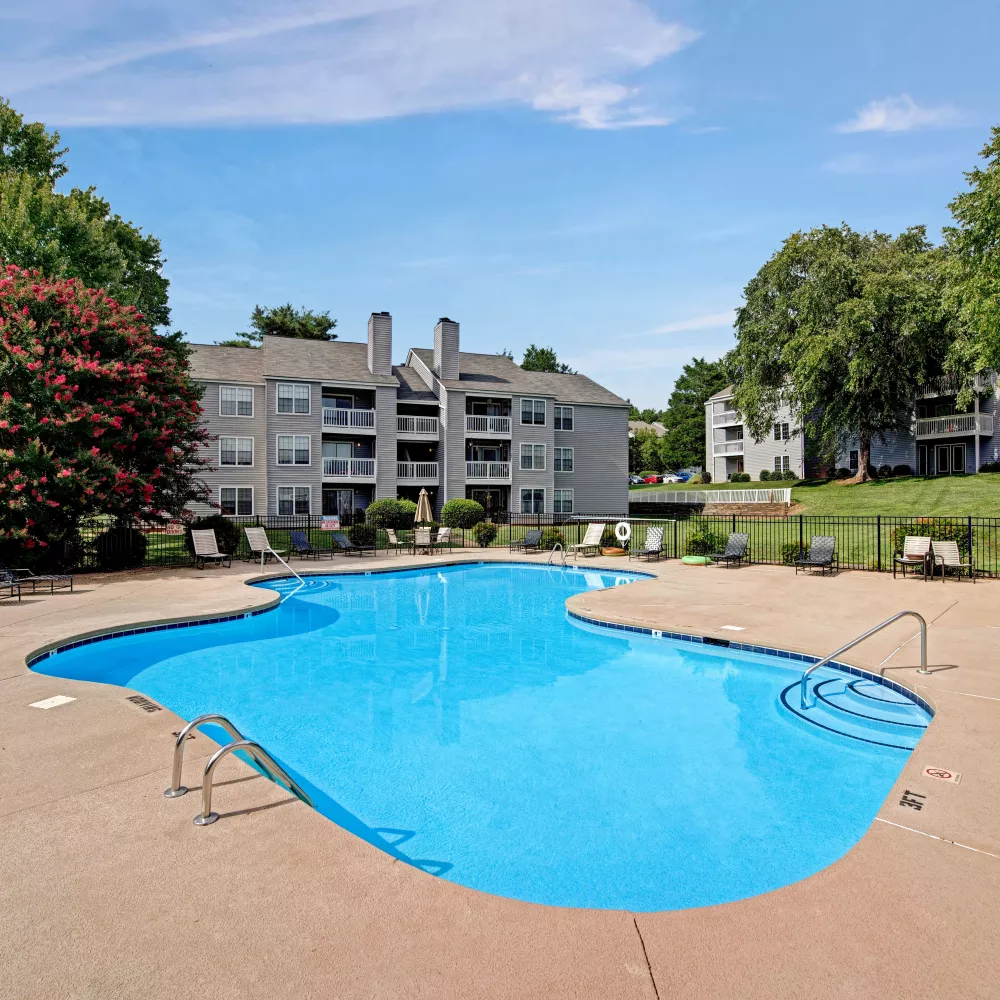 A shimmering blue pool with apartment buildings in the background, surrounded by landscaped greenery.