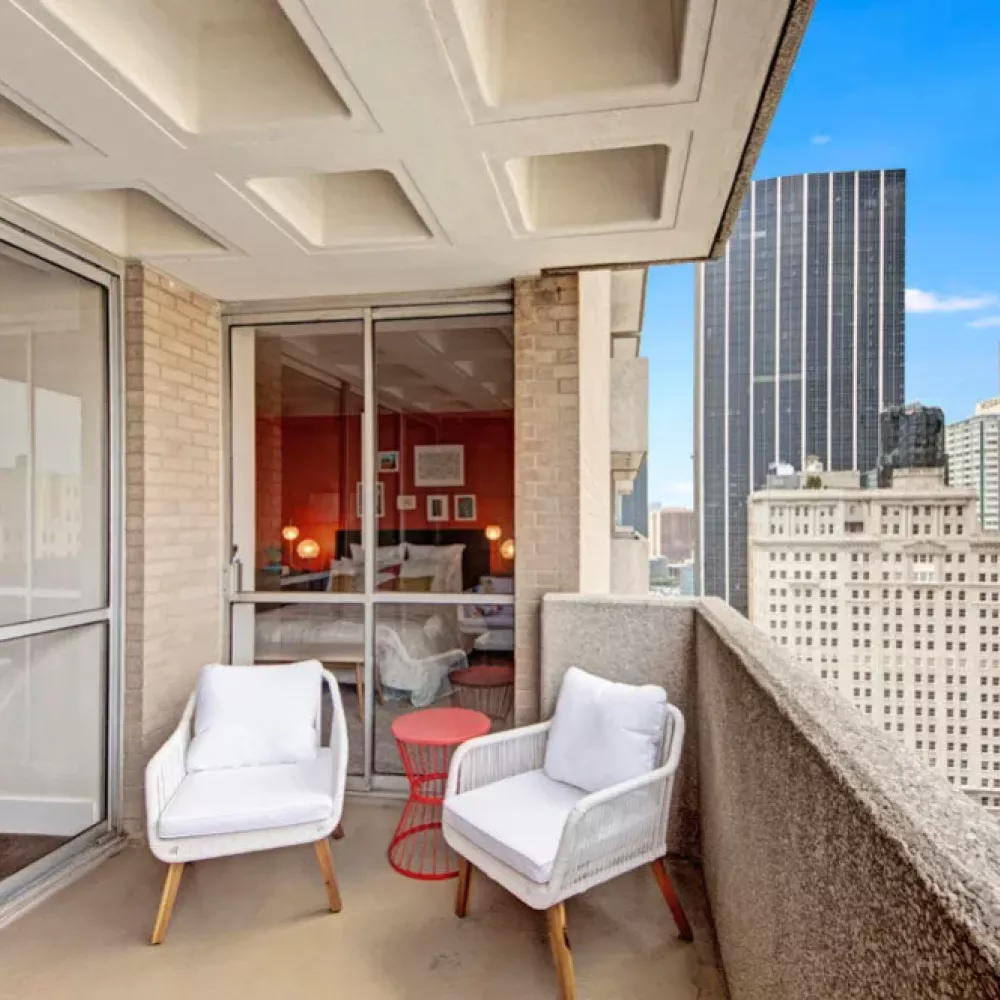  An inviting balcony featuring modern white chairs and a stunning cityscape view.