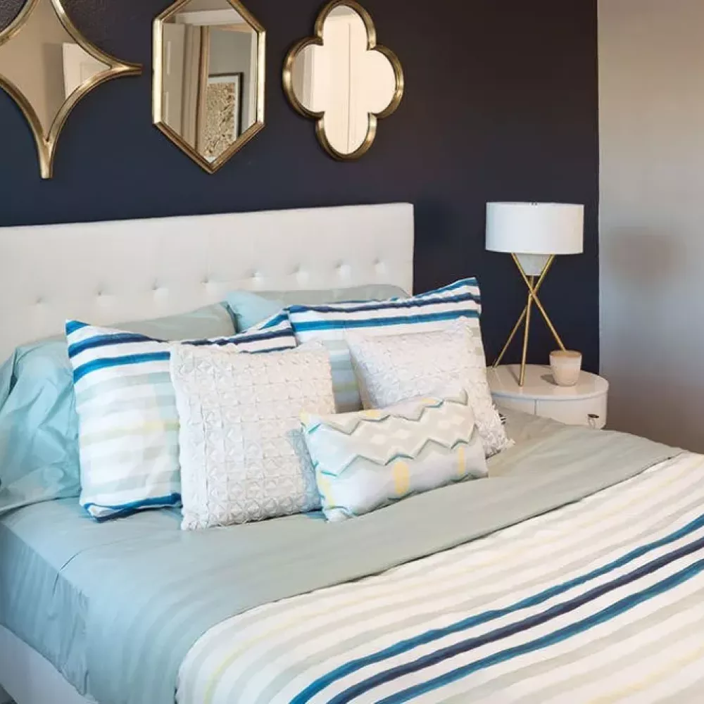 Stylish bedroom with a navy accent wall, decorative mirrors, and striped bedding on a tufted white bed.