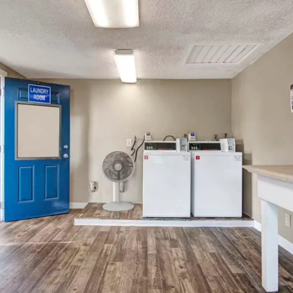 A spacious laundry room with a blue entrance door labeled "Laundry Room," showcasing two white dryers and folding areas.