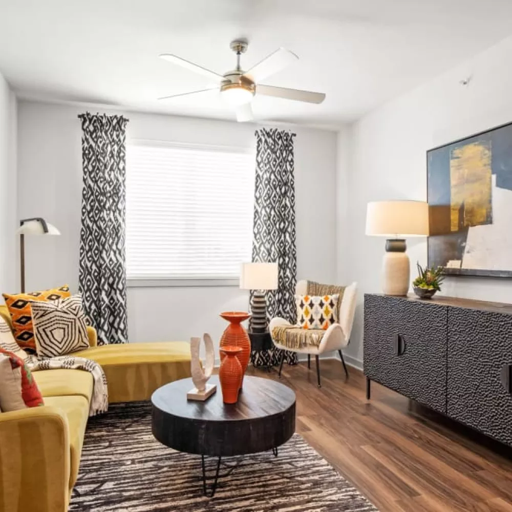 A modern living room featuring a yellow sectional sofa, patterned curtains, and abstract artwork on the walls.