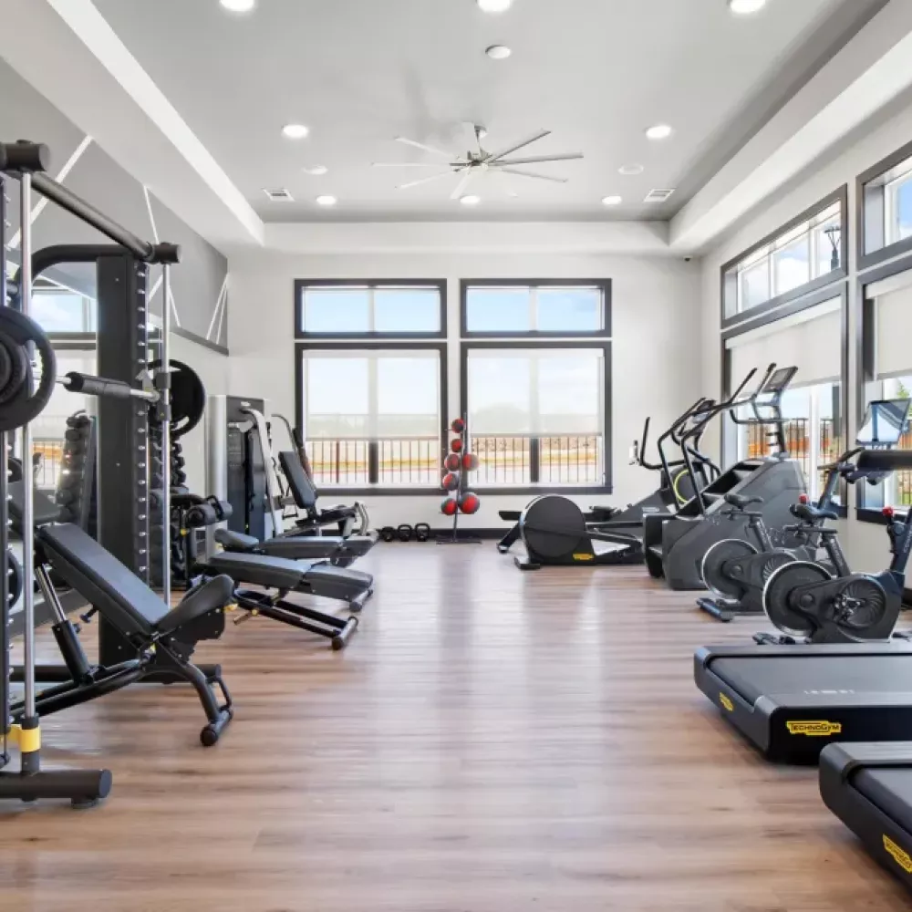 Another angle of the fitness center, featuring weight benches, ellipticals, and exercise balls under ample natural light.