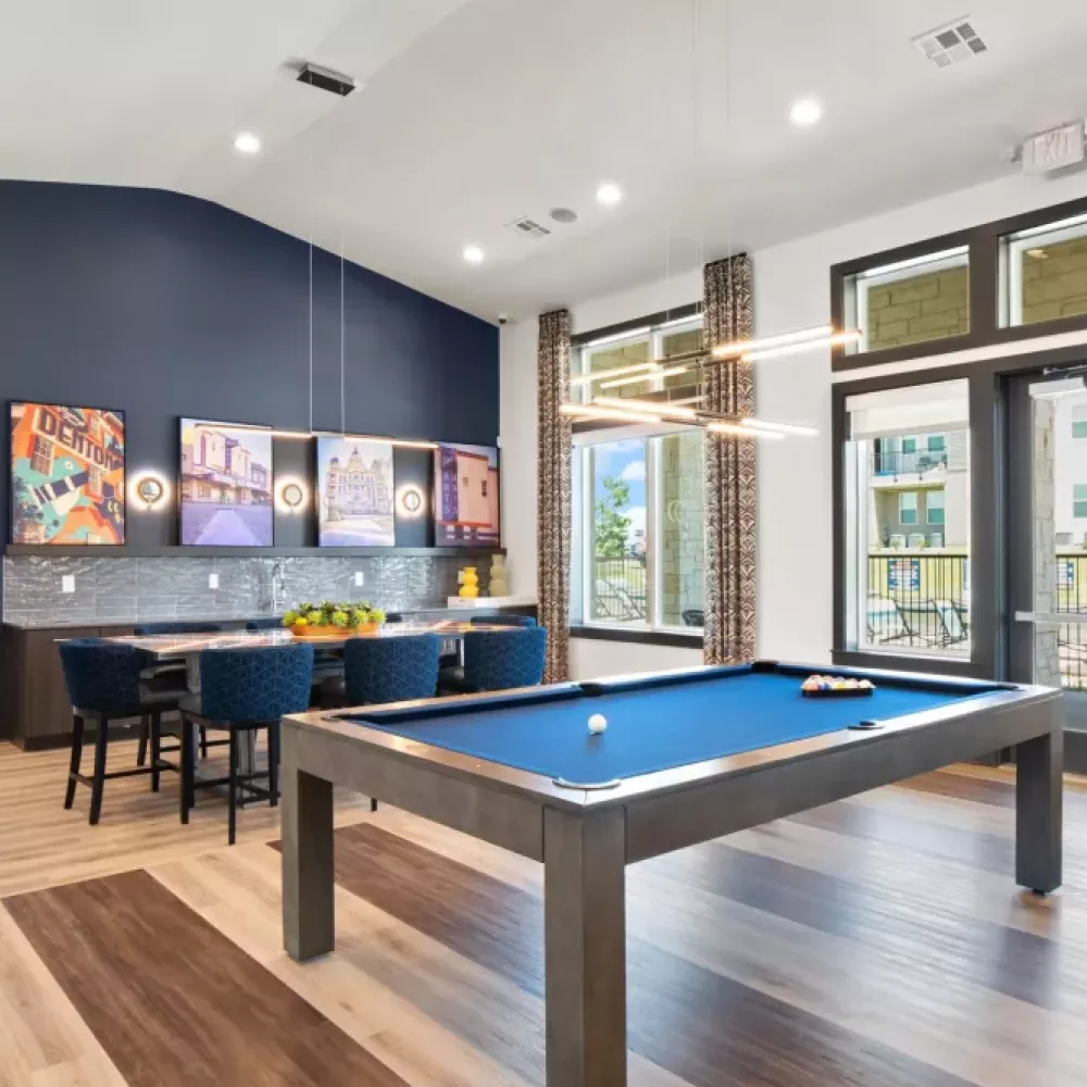 A stylish entertainment space featuring a pool table, dining table, and vibrant artwork on the navy accent wall, with ample natural light through floor-to-ceiling windows.