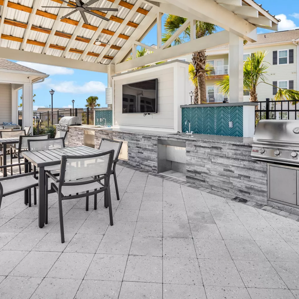 Outdoor covered patio with built-in grills, blue tiled counter with TV, and dining tables for guests.