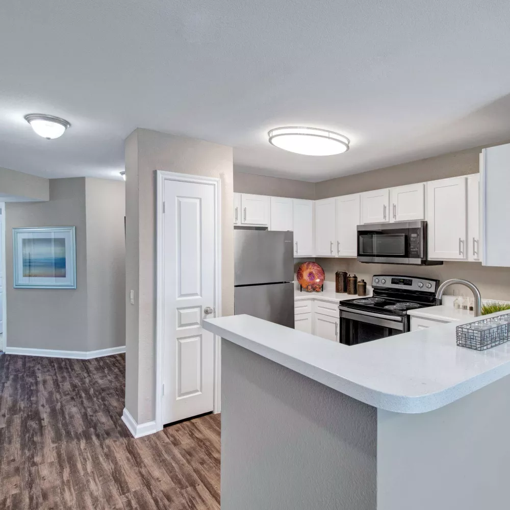 Modern kitchen with stainless steel appliances, white cabinets, and wood-style flooring.