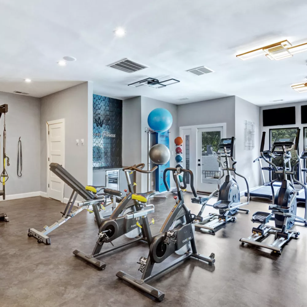 Modern gym interior with spin bikes, a weight bench, dumbbell rack, and various cardio machines.