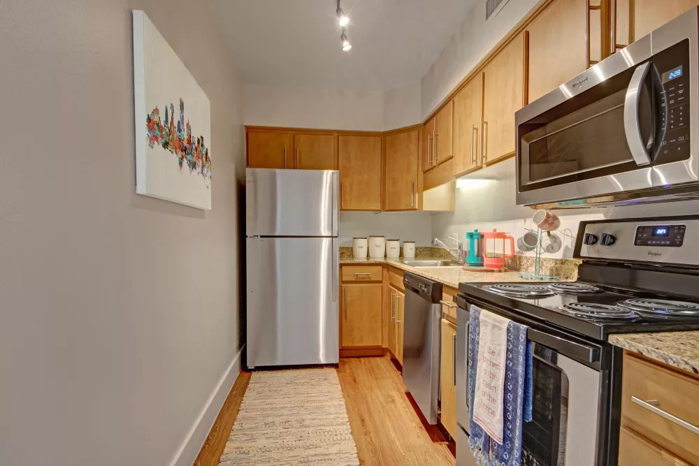 A compact kitchen with stainless steel appliances, wooden cabinets, and a decorative wall painting of a cityscape.