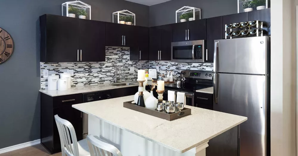 Modern kitchen with dark cabinets, stainless steel appliances, and a decorative backsplash, featuring a white island with stools.