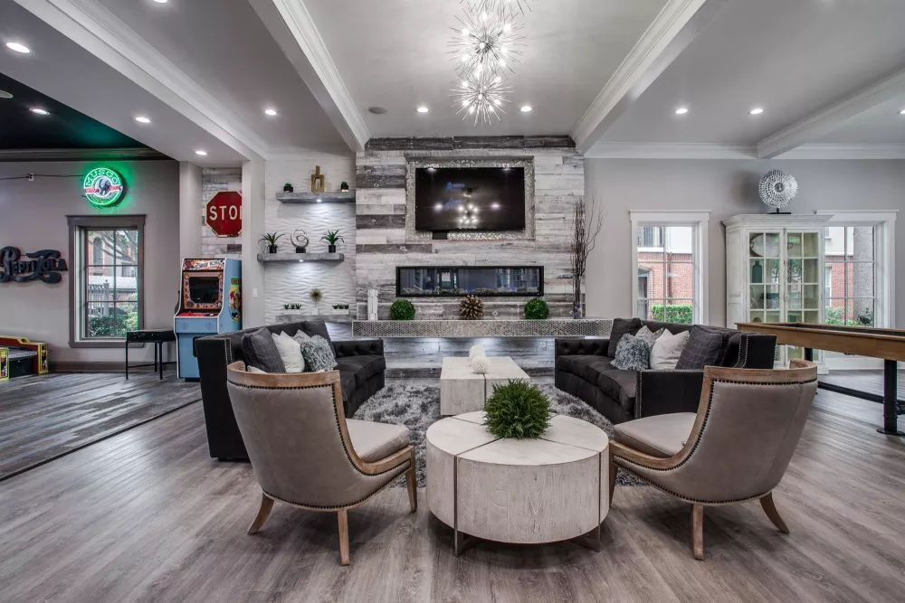 Modern lounge area with stylish seating, a fireplace with a mounted TV, and a colorful gaming zone to the left.