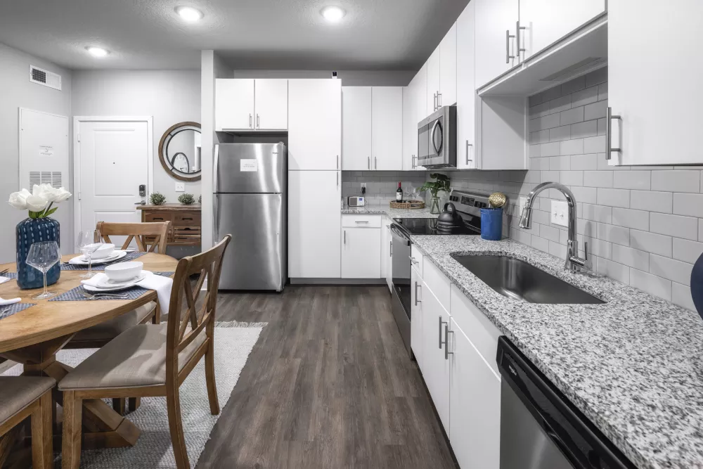 Modern kitchen with white cabinets, stainless steel appliances, granite counters, and a dining table with chairs.