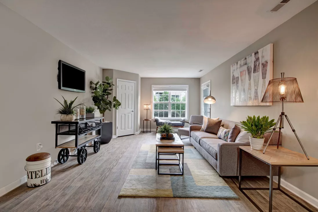  Spacious living room with modern furnishings, neutral tones, and natural light from a large window, creating a cozy and stylish space for relaxation and entertaining.