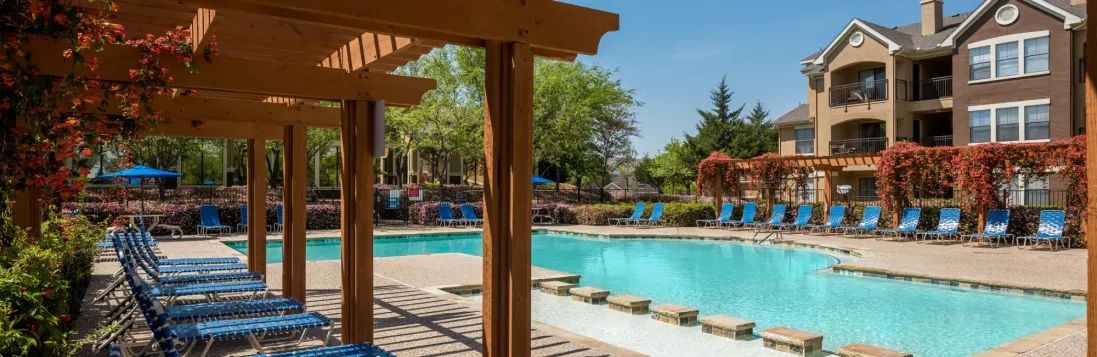 A serene pool area surrounded by lounge chairs, pergolas, and blooming greenery at a residential community.