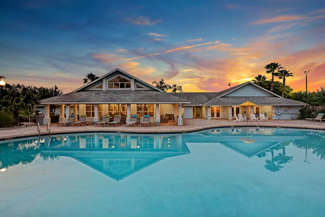 Beautiful clubhouse with large windows and a relaxing pool area at sunset, offering a welcoming ambiance.