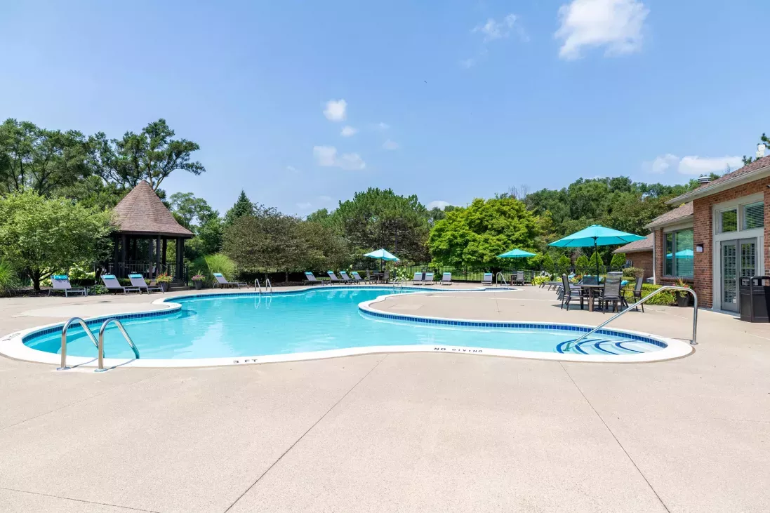 Outdoor swimming pool with blue water, concrete deck, lounge chairs, a gazebo, and a pool house under a clear sky.