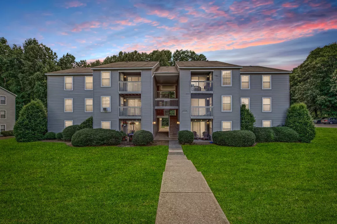 A three-story apartment building with balconies and manicured greenery at sunset at 200 Braehill Apartments.