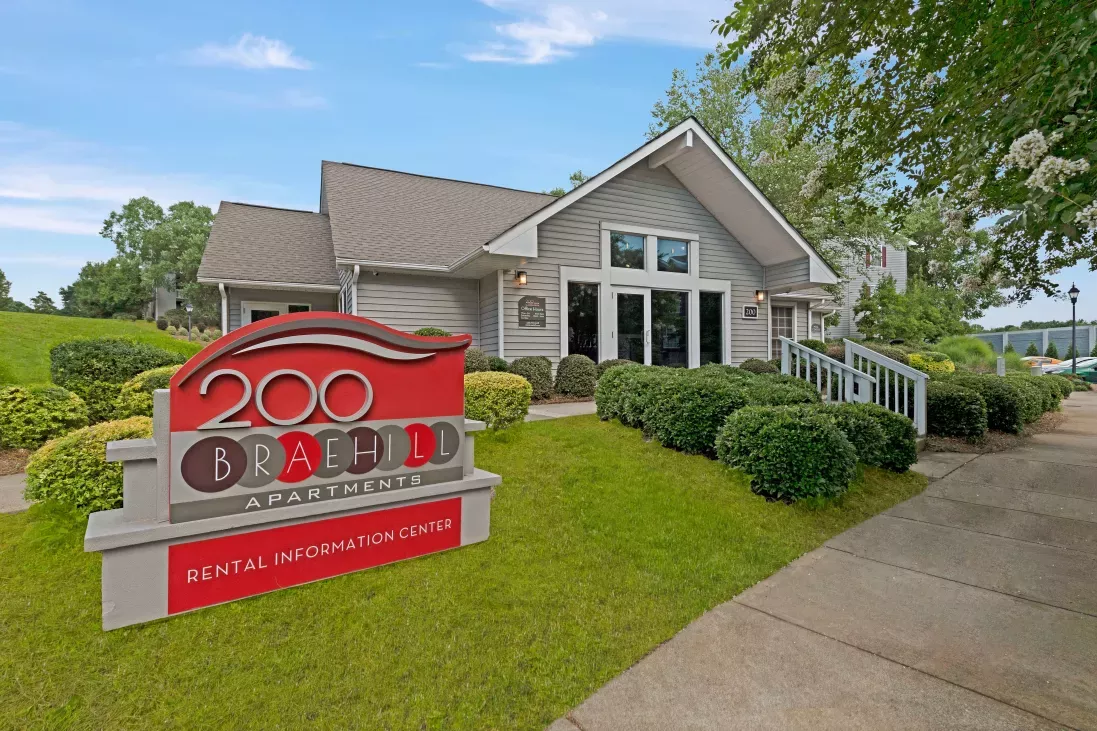 The main entrance and rental information center of 200 Braehill Apartments, featuring a red sign and well-maintained landscaping.