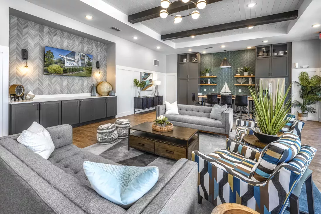 Stylish common room with grey sofas, patterned armchairs, wood coffee table, TV on a chevron wall, and dining space.
