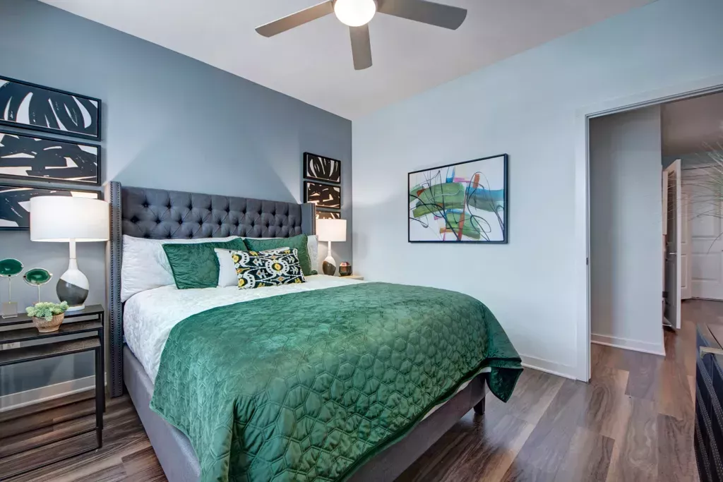 Spacious bedroom at 32Hundred Windsor Apartments in Denton, TX, featuring modern furniture, a tufted headboard, wood-style flooring, abstract wall art, and designer lighting